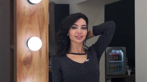 Young Attractive Girl Straightens Curls of Hair with Hands While Standing Near the Mirror in a alt