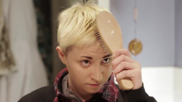 A short haired person struggling with brushing their hair just right. alt