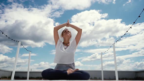 Portrait of Young Woman Sitting in Lotus Pose and Putting Hands in Namaste alt