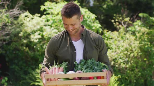 Portrait of caucasian man carrying a wooden tray full of vegetables in the garden alt