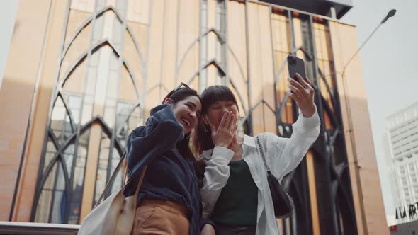 Happy two young women using smartphone video calling her friend while standing on city street. alt