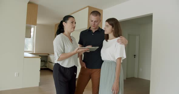 Couple Viewing New Apartment With Real Estate Agent Using Digital Tablet