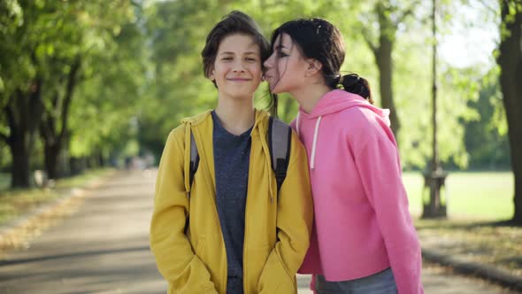 Portrait of Satisfied Teenage Boy Looking at Camera Smiling As Girl Approaching Kissing Cheek Posing alt