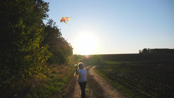 Cute Smiling Girl Jogs with Rainbow Kite on Rural Trail with Sunlight at Background alt