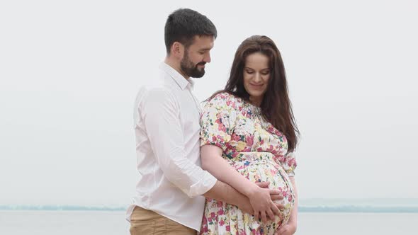 Romantic Couple In Sunny Summer Day embracing and cares pregnant woman belly