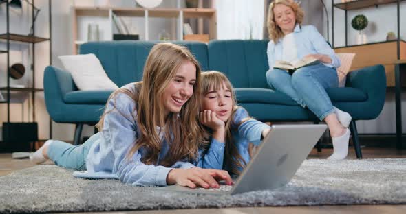Two Sisters Younger and Eldest Lying on the Floor and Use Computer alt