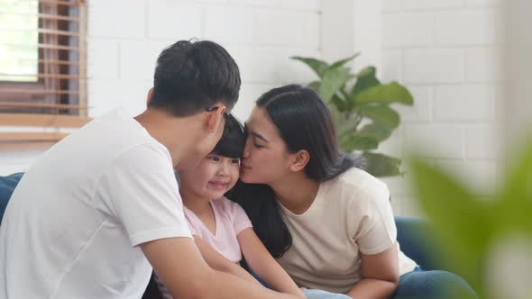 Asian family dad, mom and daughter embracing kissing on cheek congratulating with birthday at house. alt