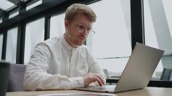 Concentrated Young Man Typing on Laptop in Cafe alt