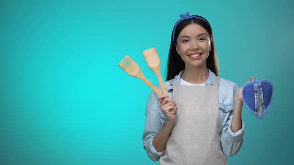 Housewife in Apron Holding Kitchenware and Smiling at Camera alt