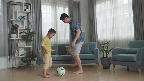Happy Asian Father And His Son Playing Soccer In Living Room alt