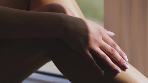 young lady strokes bare legs by manicured hand near window alt