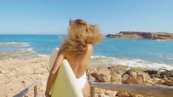 Rear View of Attractive Surfer Girl, Walking on Beach with Surfboard alt