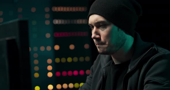 Concentrated Hacker in Sweatshirt and Cap Breaks Into Corporate Servers From His Underground Hideout alt