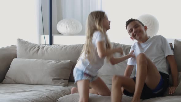 Brother Cheerfully Tickles Little Sister Funny Kids Son Daughter Laughing Together on the Couch