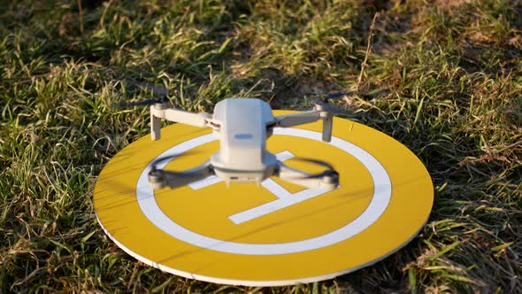Quadcopter Lands On Yellow Platform. Landing Place In The Grass. Sunny Day.Back View