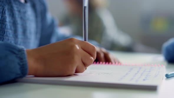 Girl Writing in Notebook at Desk in Classroom alt