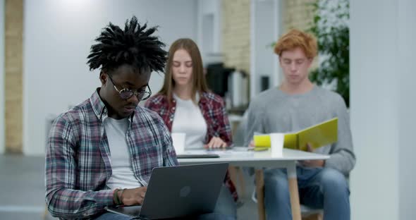 Absorbed African American Office Worker Typing on Laptop Keyboard, Looking at Camera and Smiling alt