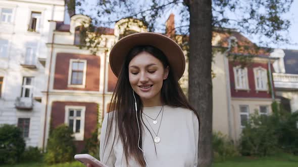Young Woman in Lovely Hat Walking Near Beautiful House and Listening Music alt