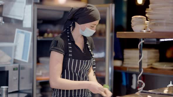 Young Female Cook in Apron and Covid19 Face Mask Preparing Ingredients for Fridge in Restaurant alt