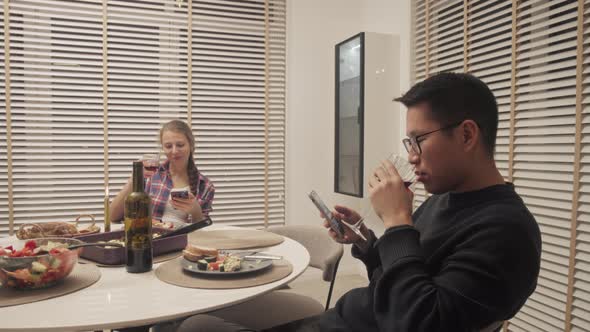 Multi ethnic couple using cellphones during dinner