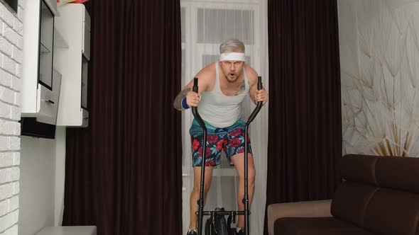 Sportsman Retro Guy in Funny Clothes Making Sport Workout Fitness Cardio Exercises on Orbitrek Home alt