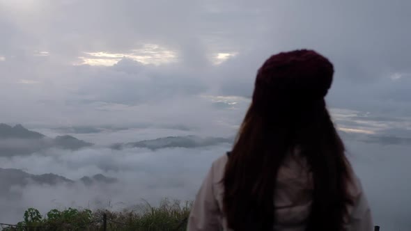 Slow motion rear view of a female traveler looking at a beautiful mountain on foggy day