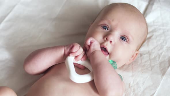A Newborn Baby Lies on Napkin on Back with a Toy in Hands and Tries To Nibble It alt