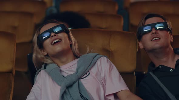 young caucasian couple laughing while watching 3D movie in movie theater.