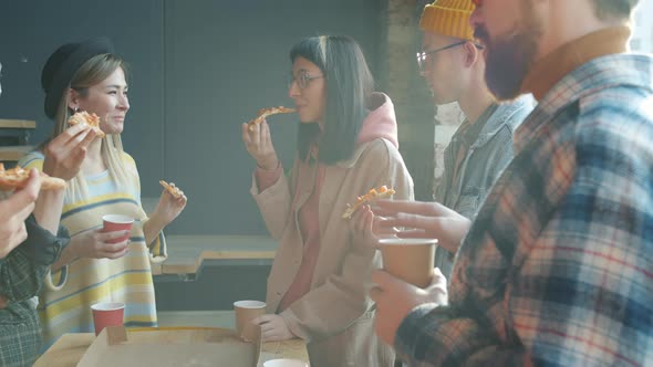 Multiracial Group of Young People Talking and Eating Pizza in Workplace During Lunch Break alt