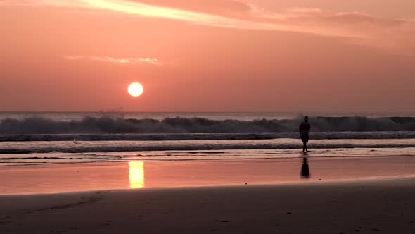 Sunset at Playa Maderas beach in Nicaragua with man throwing stones at the surf, Handheld wide shot alt