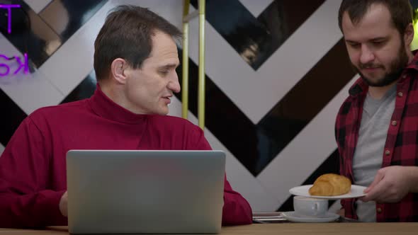 Waiter Brings Coffee and Croissant to Handsome Middleaged Freelancer in Cafe