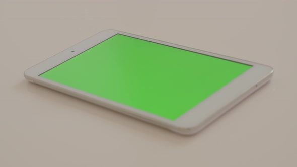 Silver tablet PC with green screen display on white reflective background 4K 2160p UltraHD footage - alt