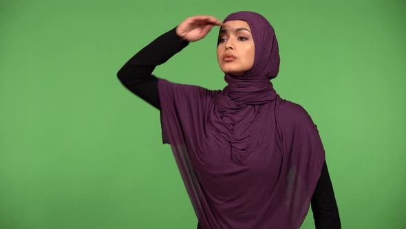 A Young Beautiful Muslim Woman Shades Her Eyes with Her Hand and Looks Around  Green Screen