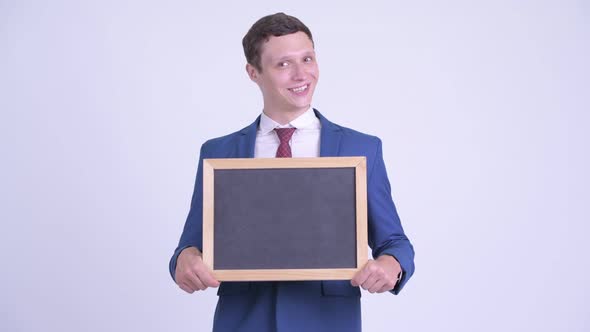 Happy Young Businessman Holding Blackboard and Looking Surprised alt