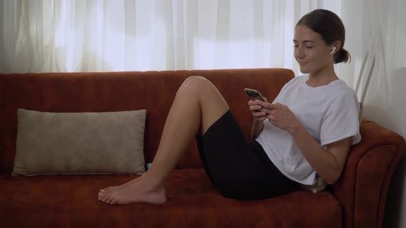 A Girl Communicates on Her Phone Sitting on the Couch at Home