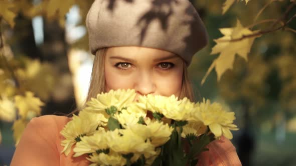 Woman with bouquet of chrysanthemums looks at camera and smiles on background autumn park.