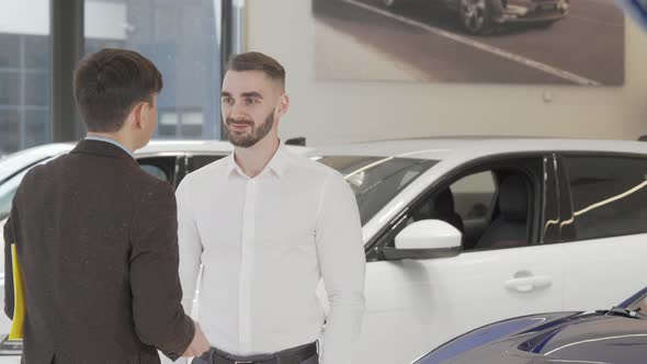 Happy Young Man Receiving Car Keys to His New Auto From the Salesman alt