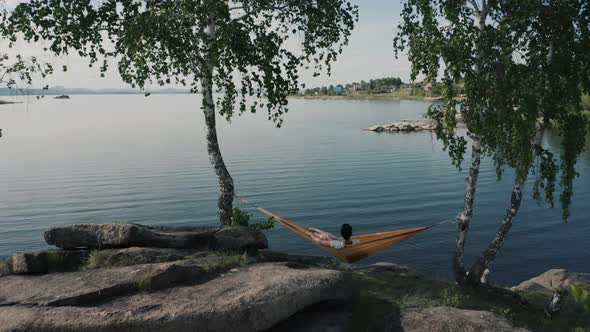 Girl Sitting in Yellow Hammock Opposite Beautiful Blue Lake