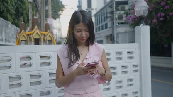 Asian Girl is Standing on the Street Laughing and Chatting on Her Mobile alt