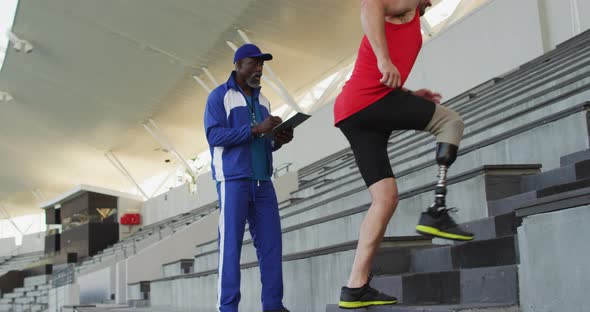 Diverse male coach and disabled athlete with prosthetic leg training, running up stairs alt