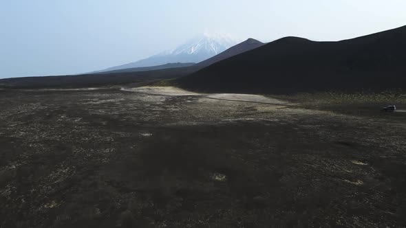 cars drive on black earth overlooking volcanoes