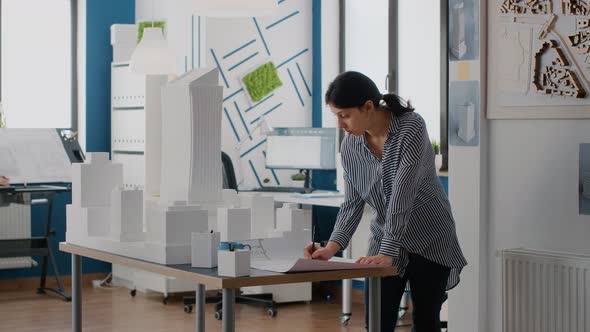 Contractor Holding Building Model to Design Blueprints Plan on Table alt