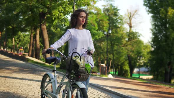 Young Woman in a White Tshirt and Blue Jeans Walking on the Cobblestone Road in the City Park alt