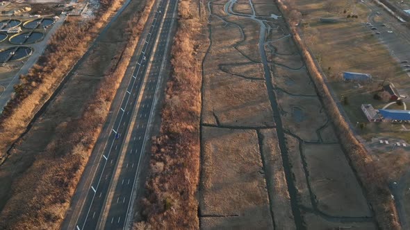 An aerial view high over a marsh on Long Island, NY. A long road with a few cars run next to it, sho alt