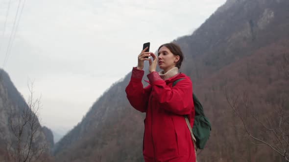 A Girl in a Red Raincoat Walks and Takes Photos of the Mountains