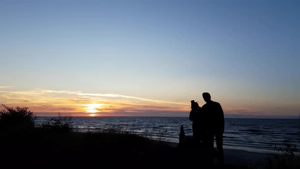 Young couple watching sunset on the beach. Only silhouettes visible. Colorful sunset. Man and woman alt