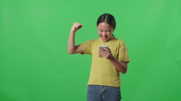 Young Asian Kid Girl Surprise And Say Wow During Use Mobile Phone While Standing On Green Screen alt