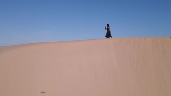 Two Woman Seen Walking Along Edge of Sand Dune