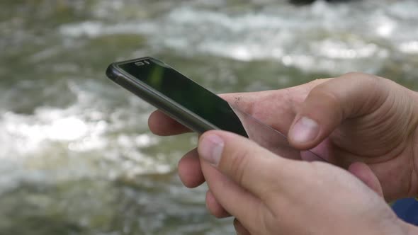 Unrecognizable Male Traveler Hands Using Smartphone on Mountain Creek Background