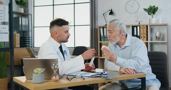 Male Worker Speaking with Old Man, Giving Pills and Explaining Treatment During Medical Visit alt